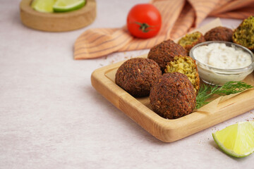 Wooden board with delicious falafel balls, sauce and lime on light background, closeup
