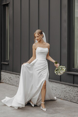 A woman in a white wedding dress is walking down a street holding a bouquet of flowers. Concept of...