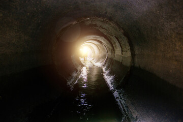 Dirty sewage flowing in round underground sewer tunnel