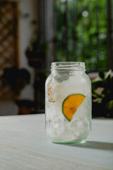 sweating glass cup with ice cubes and half a slice of lime on light wooden board table 