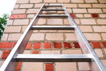 A stepladder against the wall of a brick private house. Household work, manual labor, climbing stairs.