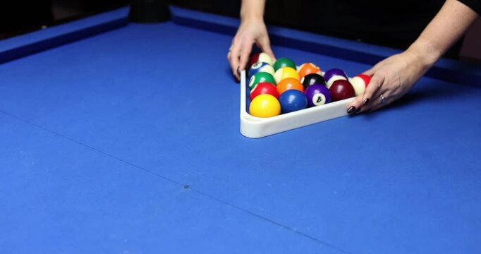 Female hands arrange billiard balls in form of equilateral triangle. Woman with black manicure uses triangular frame before new billiard game