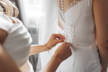 A woman in a white dress sits on a bed. She is wearing a white veil and has her hair in a bun