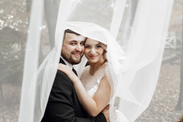 A bride and groom are posing for a picture under a white veil