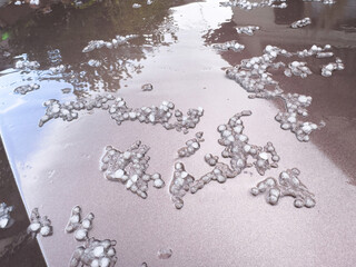 Hailstones on maroon topaz-colored car bodywork after a tempest, showcasing the aftermath of the...
