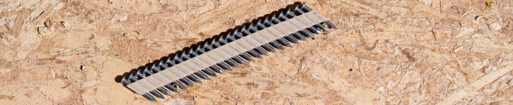 Construction background, collated nail gun nails, connected with paper tape; on a sheet of oriented strand board, OSP, wood supplies
