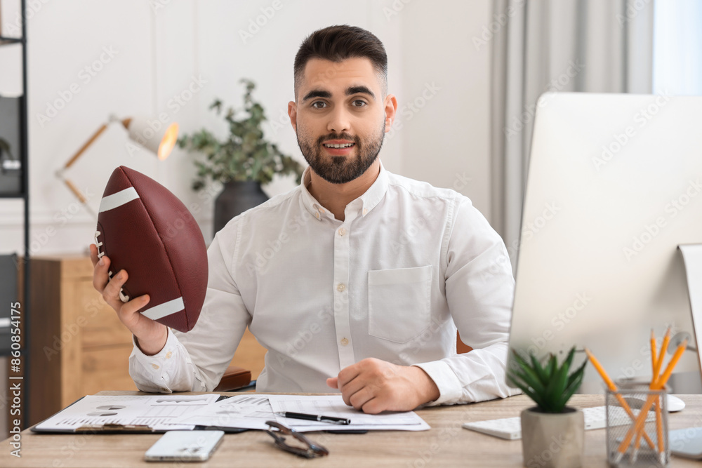 Canvas Prints Young man with american football ball at table in office