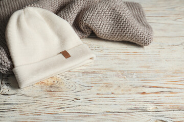 Gray knitted scarf and hat on wooden table, space for text