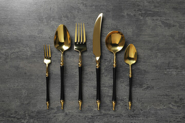Elegant golden cutlery set on dark grey table, flat lay