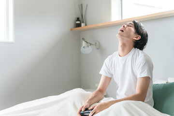 Obraz premium 家のベッドルーム・寝室でゲームをする男性ゲーマー（ゲームオーバー・負ける・悔しい・課金） 