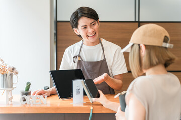 カフェのレジ・会計で電子決済・スマホ決済に対応するカフェ店員
