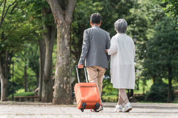 スーツケースを持って旅行する高齢者夫婦の後ろ姿（シニアライフ・アクティブシニア）
