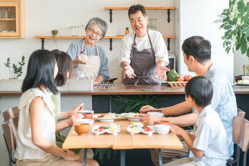 家のダイニングで家族団欒して食事する子供と夫婦・親子・三世代家族（二世帯住宅）
