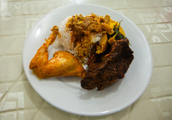 A plate of Padang Rice, served with chicken curry, fried lungs, and vegetables, a very famous specialty from West Sumatra Province, Indonesia.