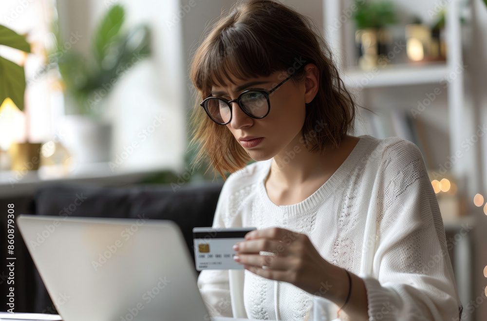 Wall mural a woman in an office holding a credit card and looking at a laptop while sitting on a desk with a wo