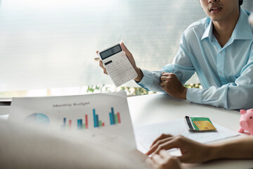 Couple Discussing Financial Plan Investment with Planner, Analyzing Monthly Budget, and Using Calculator in Modern Office Setting