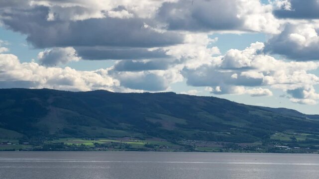 Timelapse of big summer clouds moving over Mj&oslash;sa lake on a spring day. Farmland on the other side of the lake.