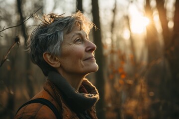 Portrait of a happy senior woman in autumn forest at sunset.