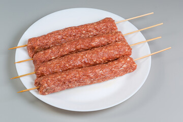 Raw lula kebab on the wooden skewers on white dish