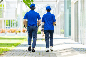 Rear view of delivery workers walking and carrying luggage in front of a building