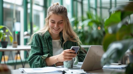 Fototapeta premium Modern Productivity: Young Woman Smiling at Smartphone While Working at Bright, Airy Table with Laptop and Coffee