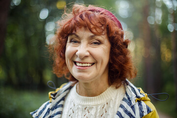Portrait of a happy elderly woman with red curly hair in the park.