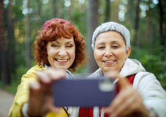 Multiracial elderly women having fun during trekking day in to the wood - make selfie with smartphone.