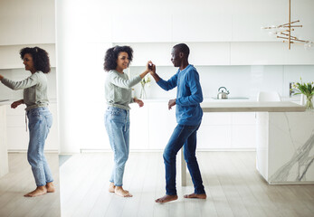 Cheerful millennial black spouses having fun together dancing to music in modern kitchen interior.