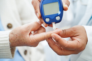 Asian doctor using digital glucose meter for check sample blood sugar level to treatment diabetes.