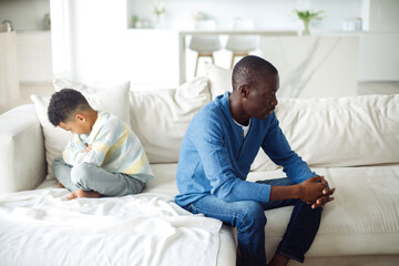 Fototapeta premium Father and son are offended by each other and sit with their backs to each other on the sofa.