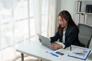 Surprised and happy businesswoman shows joyful expression after viewing news results, business approval results and financial approval results on laptop at office. Startup business growth concept.