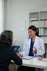Confident Asian female doctor explains and questions a retired female patient attending a private clinic for treatment and therapy. Health concept, health insurance.
