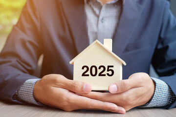 Businessman hands holding wooden House model with 2025 New Year text. Property insurance and real estate concepts