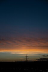 Obraz premium A sunset with an orange and blue sky over a cityscape featuring a power line tower and distant hills