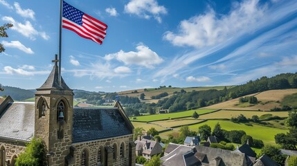 An American flag flying high above a historic stone church, with a charming village and rolling hills stretching out below