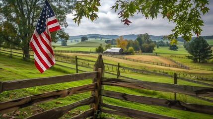 An American flag hanging from a rustic wooden fence, with a picturesque farm and rolling green fields in the background