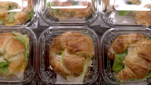 Top view of freshly made croissant sandwiches packaged in clear plastic containers, arranged in a display case at a store. High quality 4k footage