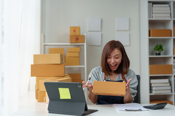 Business entrepreneur or independent Asian woman using laptop with parcel box successful I'm happy and proud of my success in my startup business. Packaging boxes, marketing and online shipping.