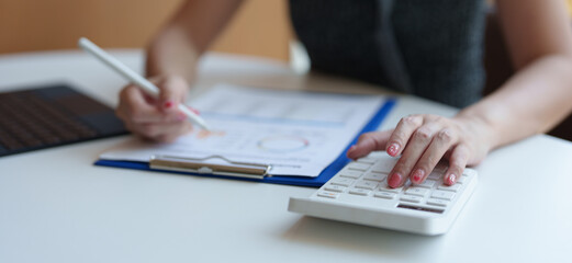 Attractive and confident Asian businesswoman sitting on desk and laptop computer Calculator for office calculations Document balance report is being prepared. Financial Accuracy, Taxes, Accounting.
