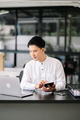 Young handsome man typing on tablet and laptop while sitting at the working tabl in office.