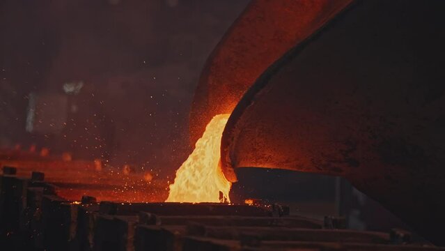 Pit pours liquid metal into molds. Stock footage. Liquid mass of molten metal pours out of pit. Stream of liquid metal is poured into molds at metallurgical plant