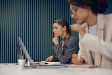 Serious female office workers working on project and use laptops sitting in coworking