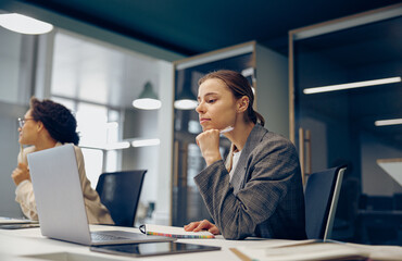 Focused business woman working on laptop while sitting the desk in office on colleague background