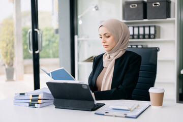 Young Arabic female entrepreneur wearing a hijab working  with a laptop Concentrated math finance on an office desk, tax, report, accounting, statistics