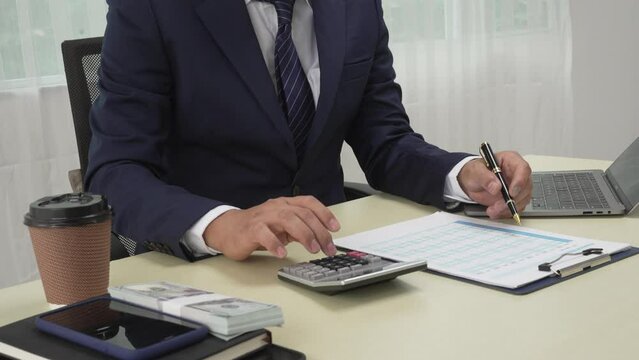 A banker in a suit works at a desk handling loans, analyzing client financial data, providing financial advice, dealing with stocks and the stock market, and studying economic situations.