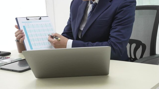 A banker in a suit works at a desk handling loans, analyzing client financial data, providing financial advice, dealing with stocks and the stock market, and studying economic situations.