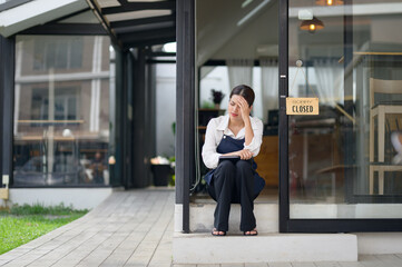Asian female coffee shop owner Stressed barista Headache and regret hanging the shop closed sign on...
