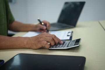 A householder manages household expenses while working at a desk, tracking various costs such as transportation, housing, groceries, dining, healthcare, utilities, and personal items to maintain