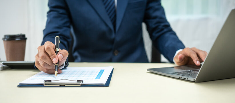 A banker in a suit works at a desk handling loans, analyzing client financial data, providing financial advice, dealing with stocks and the stock market, and studying economic situations.