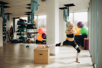 Obraz premium Athletic woman in sportswear doing squat while standing on wooden crossfit box at gym